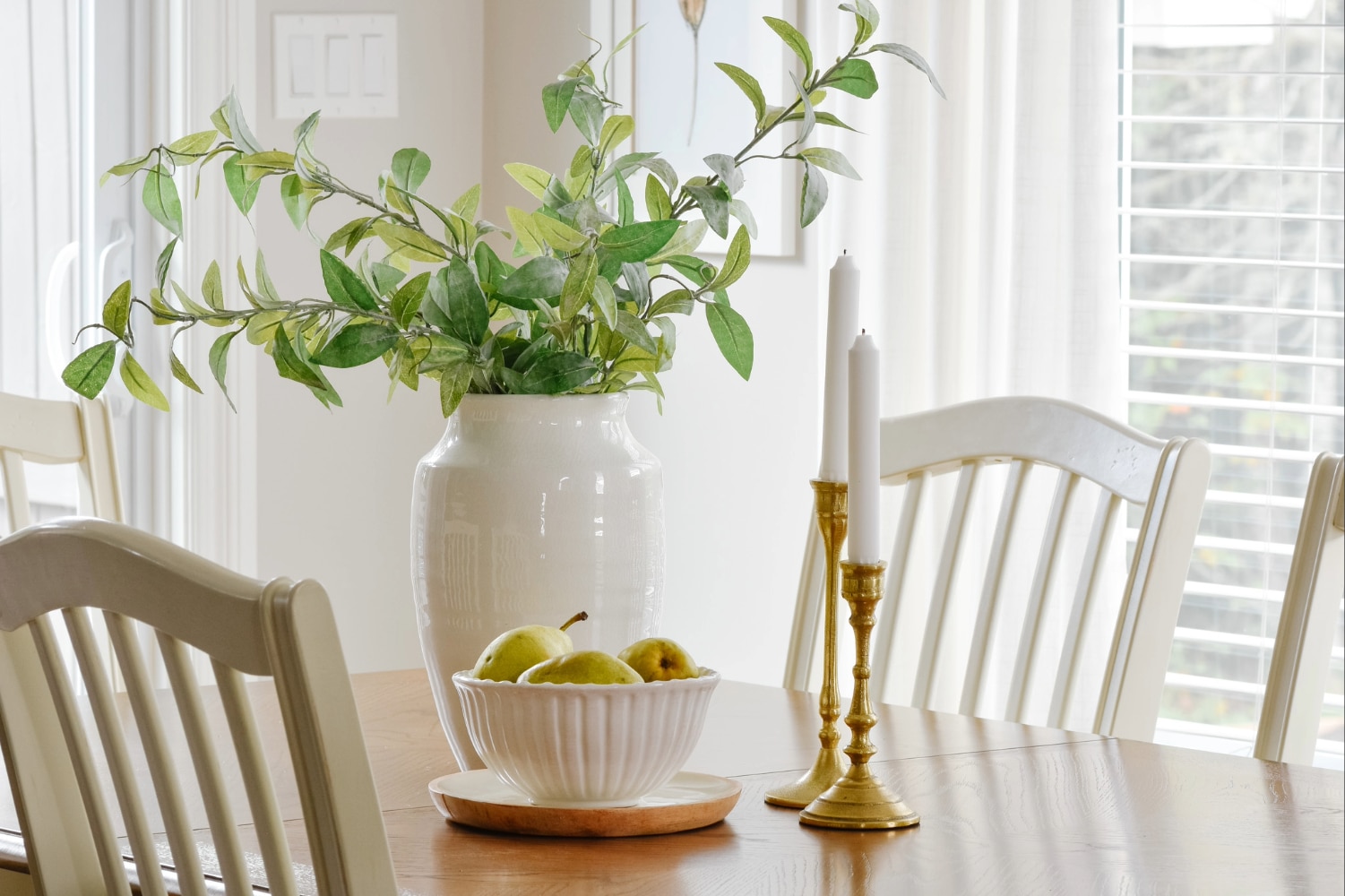 brass home decor candle sticks, vase and bowl of pears on dining room table